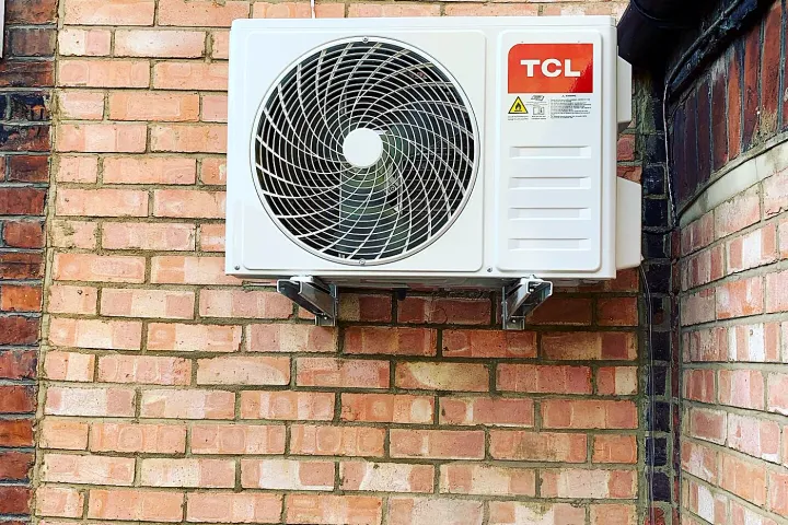 An air conditioning condenser unit mounted on an exterior brick wall