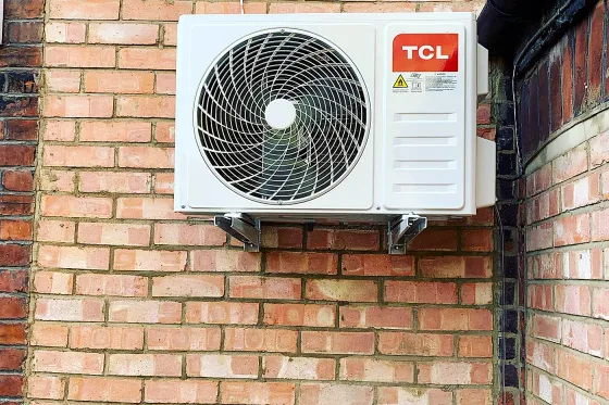 An air conditioning condenser unit mounted on an exterior brick wall