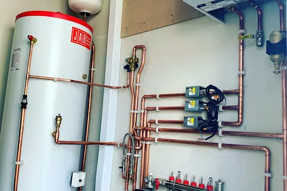 An unvented cylinder, zone valves and copper manifold in a finished plant cupboard